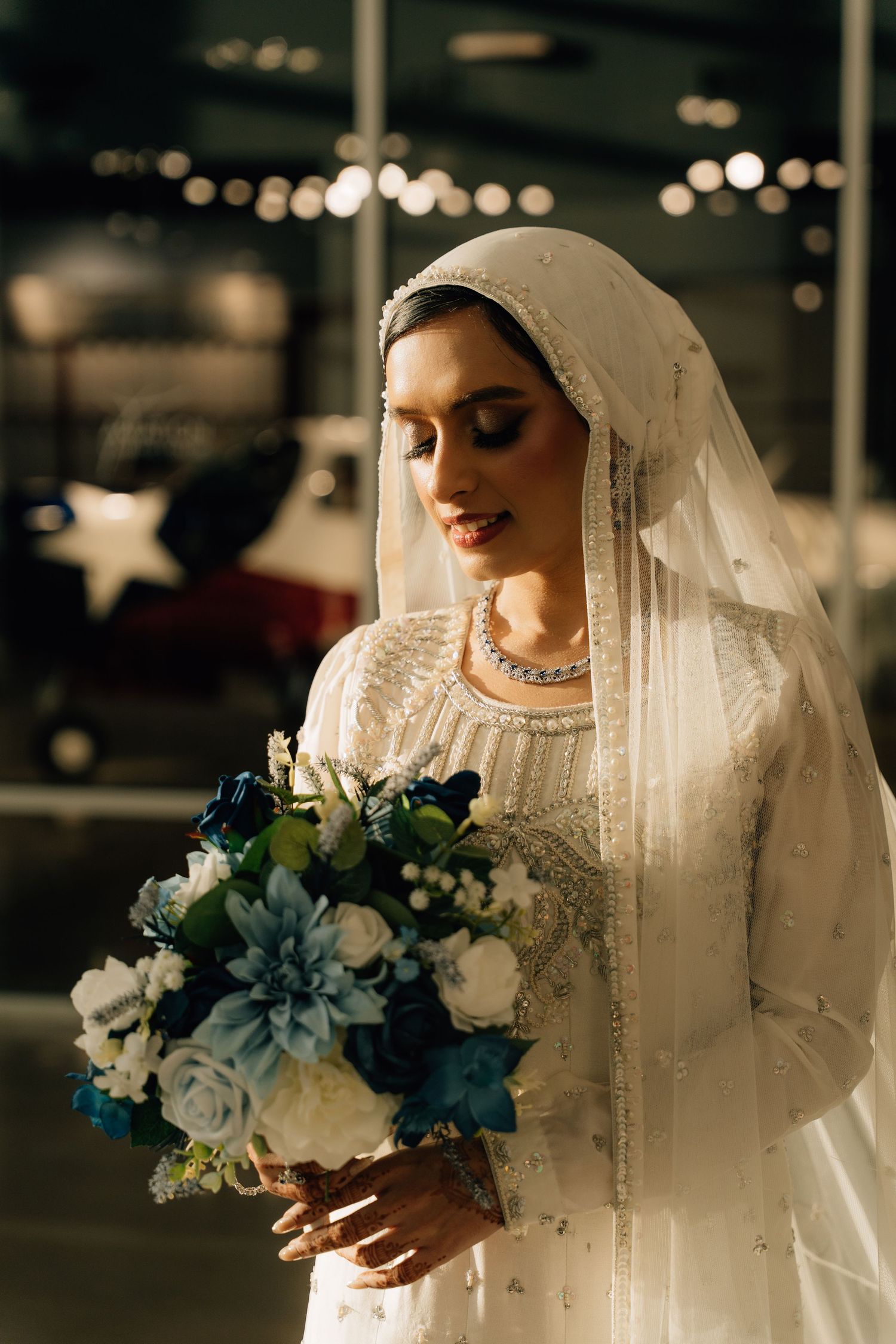 A bridal portrait with white veil and blue floral bouquet in low light setting.