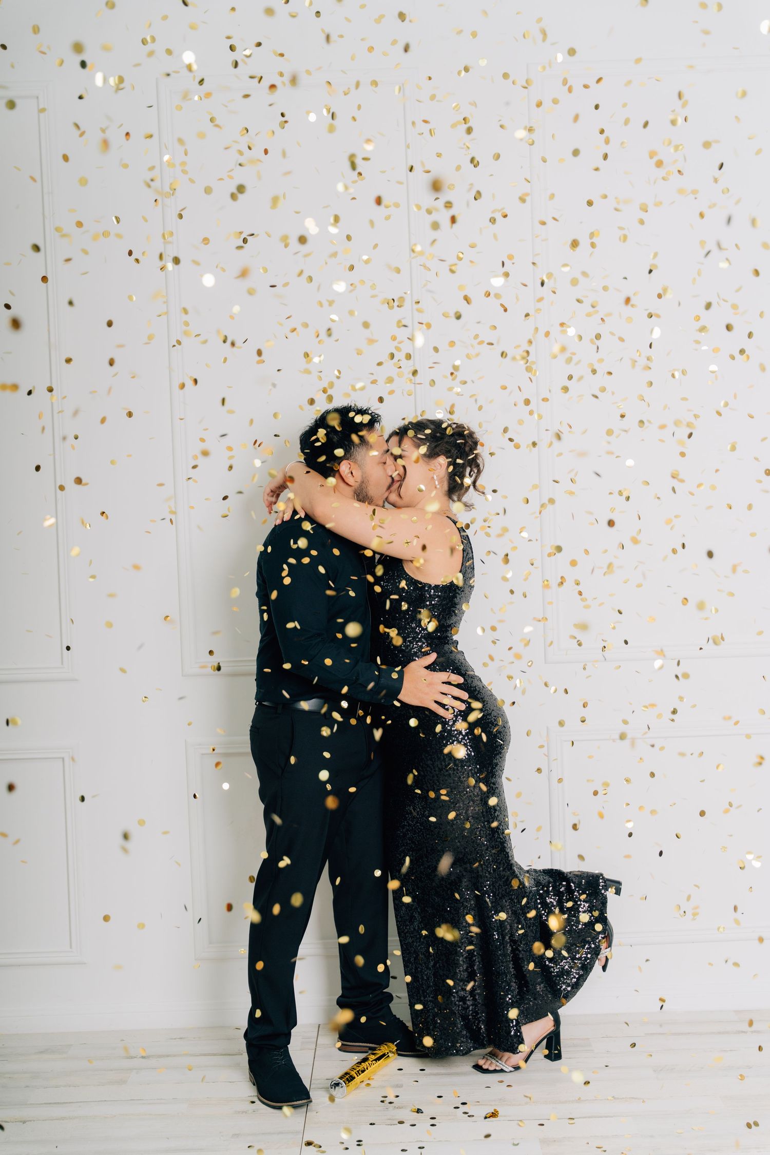 Romantic couple embracing while gold confetti falls around them against white background.