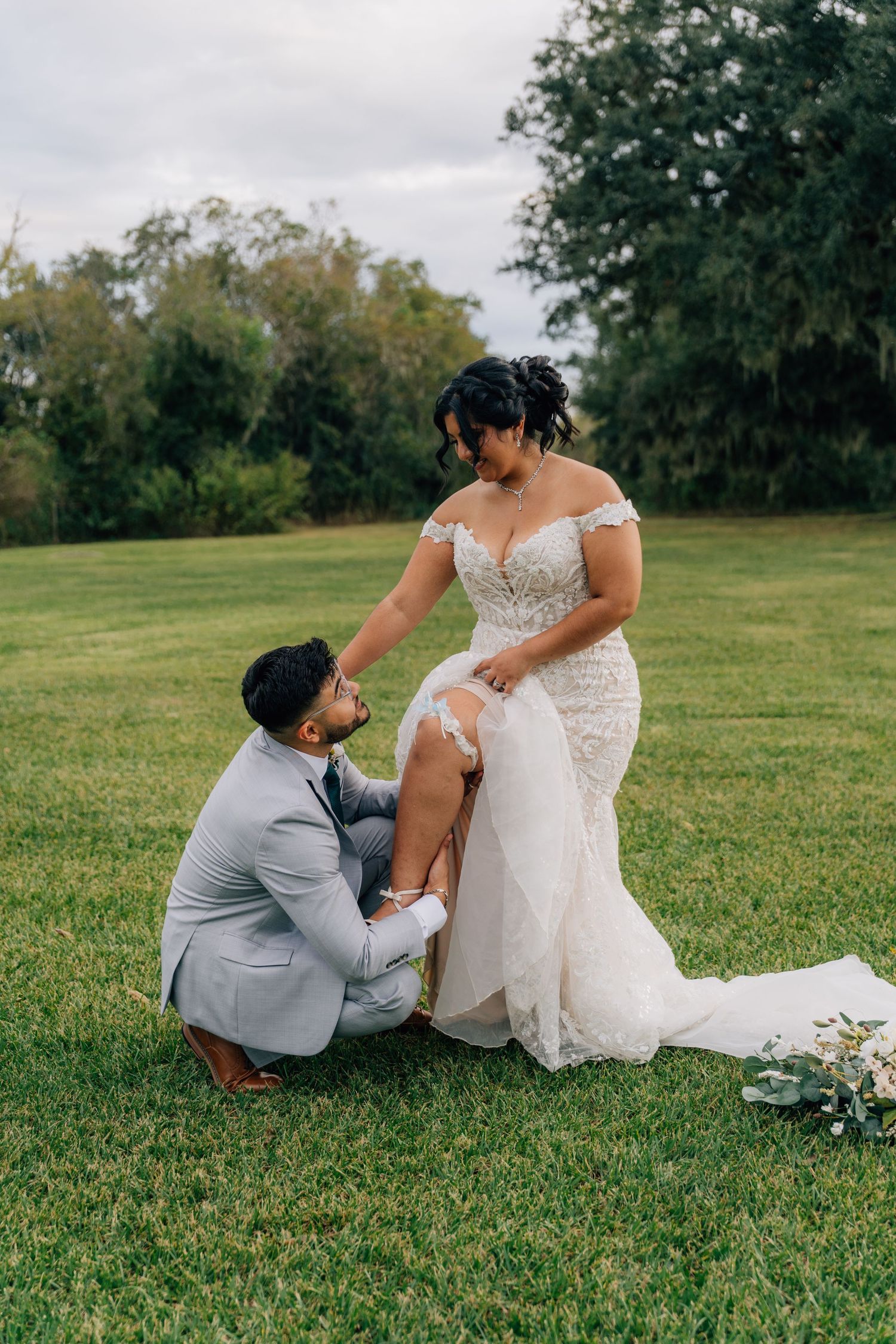 Romantic wedding moment on grassy lawn with groom kneeling before bride.