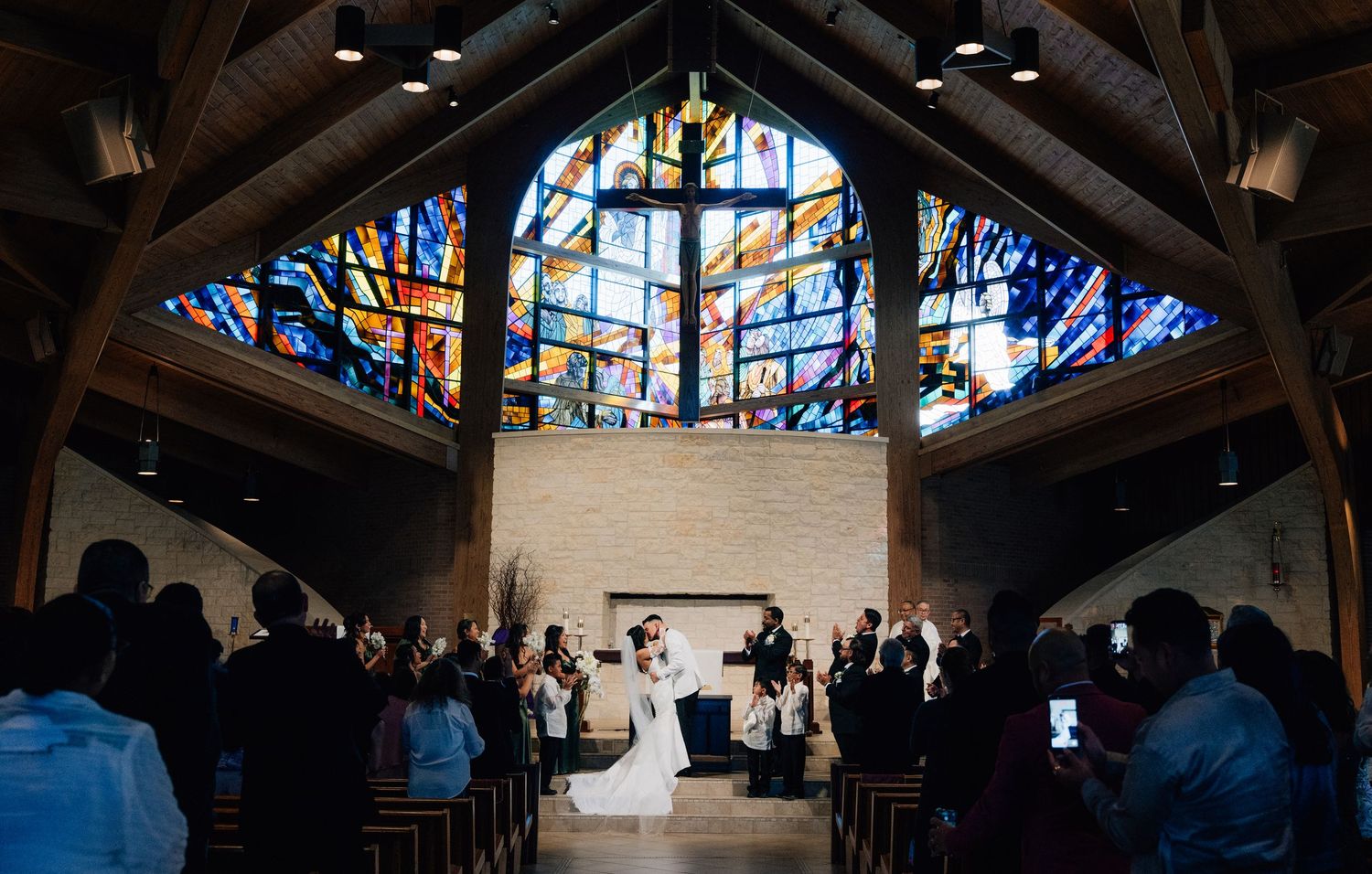 Interior of church with beautiful stained glass windows and vaulted wooden ceiling during ceremony.