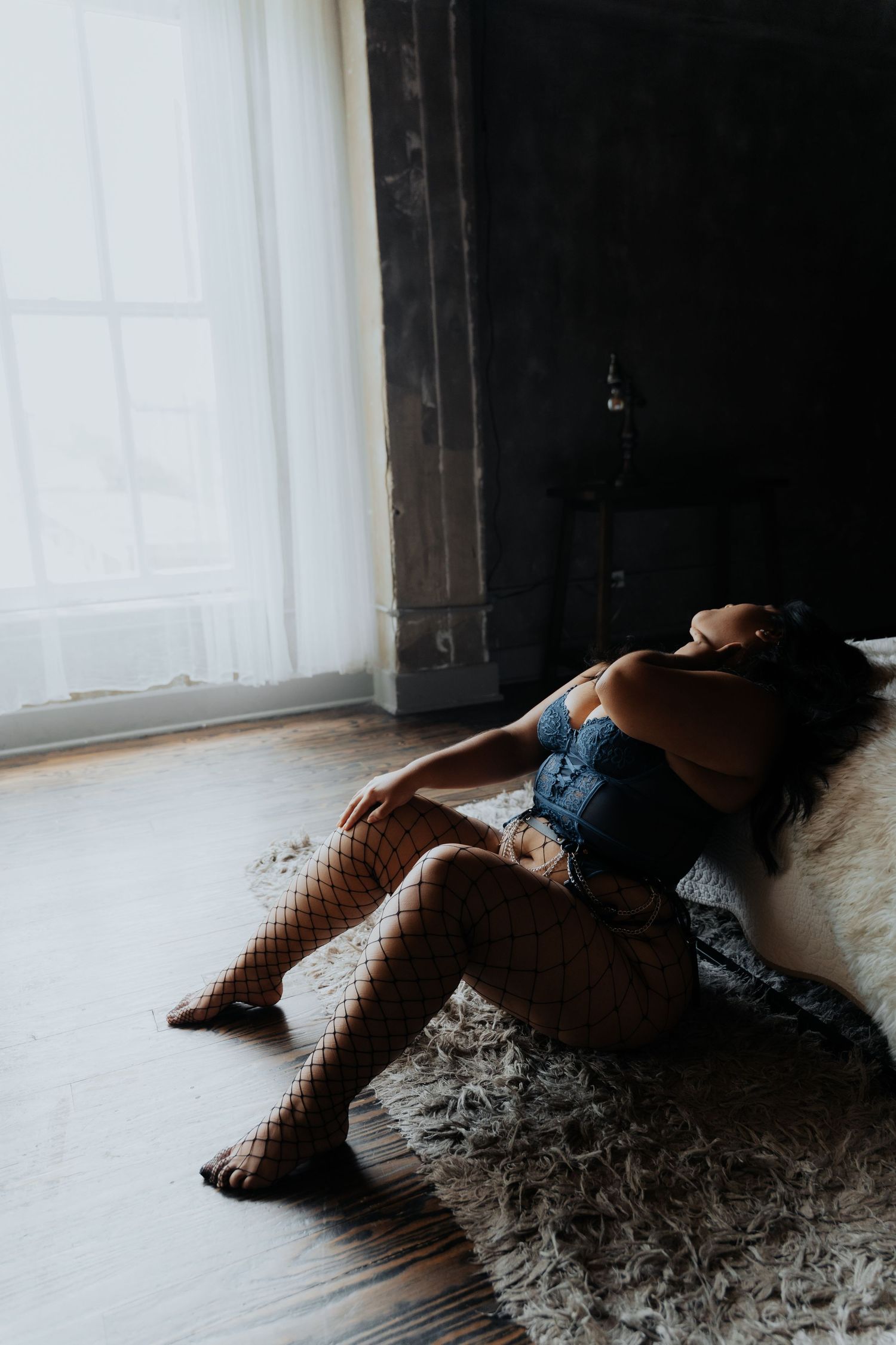 Person reclining on plush carpet near window in moody indoor setting.