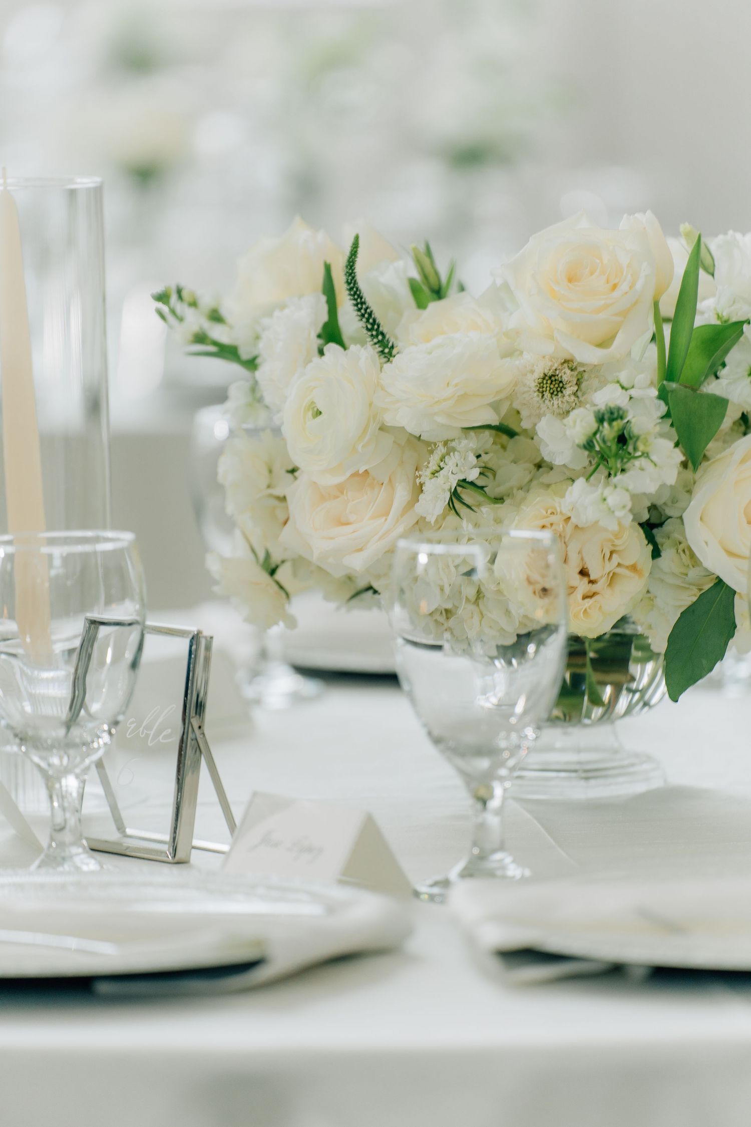 White floral centerpieces and place settings create an elegant tablescape for a formal event.