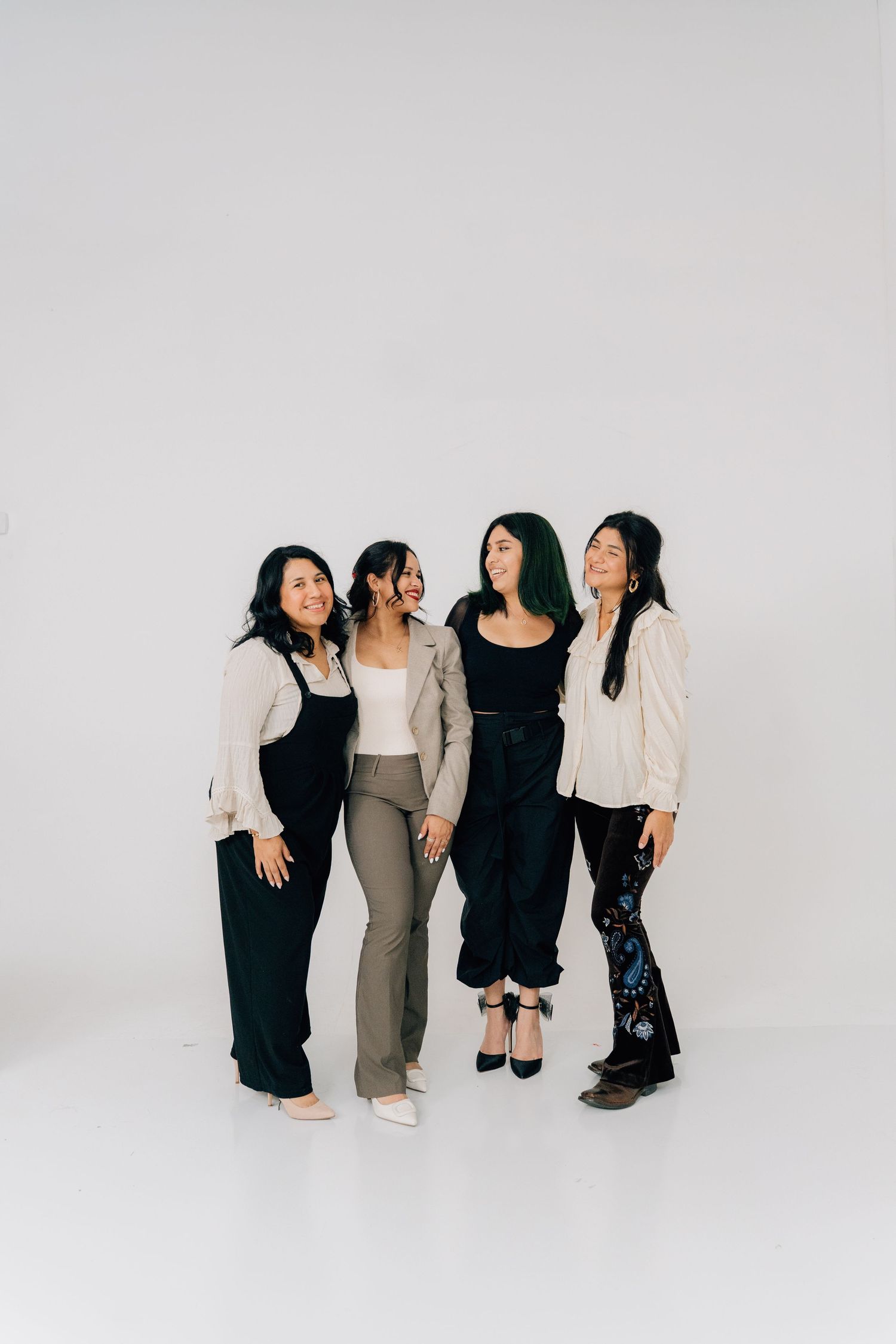 Four women stand together in stylish black, white and beige outfits against minimalist backdrop.
