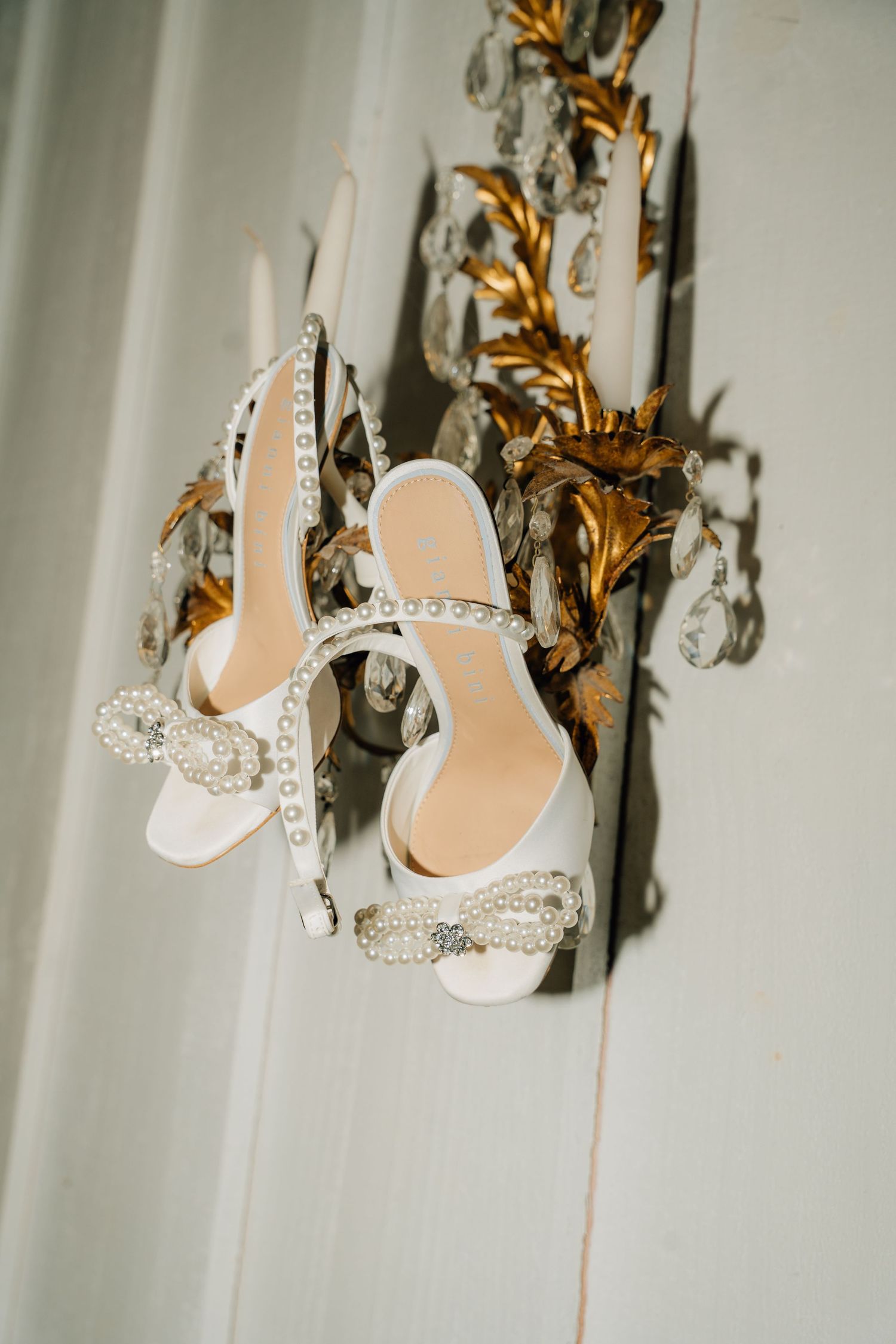 Sparkly bridal shoes with crystal details displayed on ornate gold wall sconce.