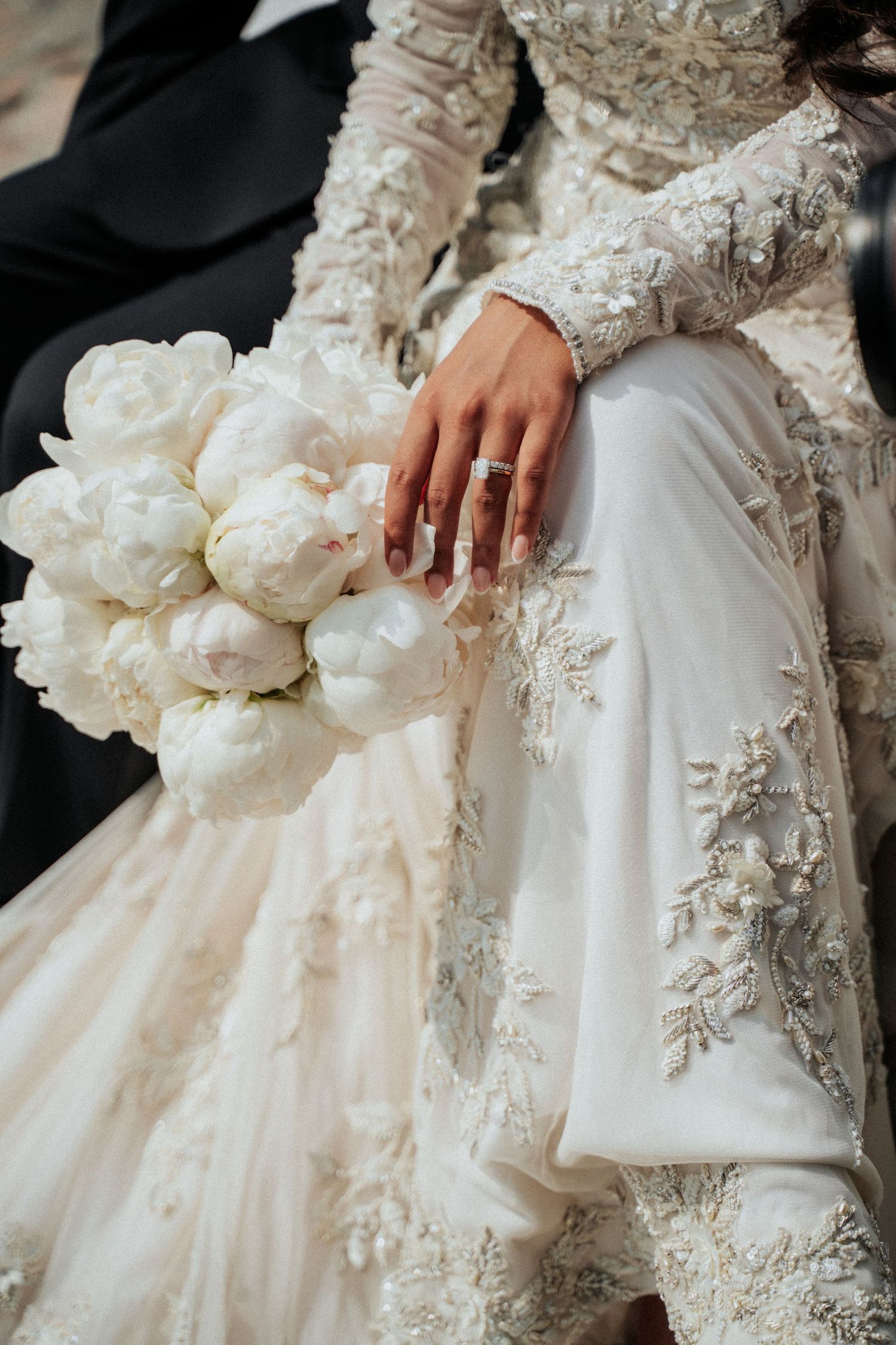 Close-up details of ornate wedding dress with lace appliques and white floral bouquet.