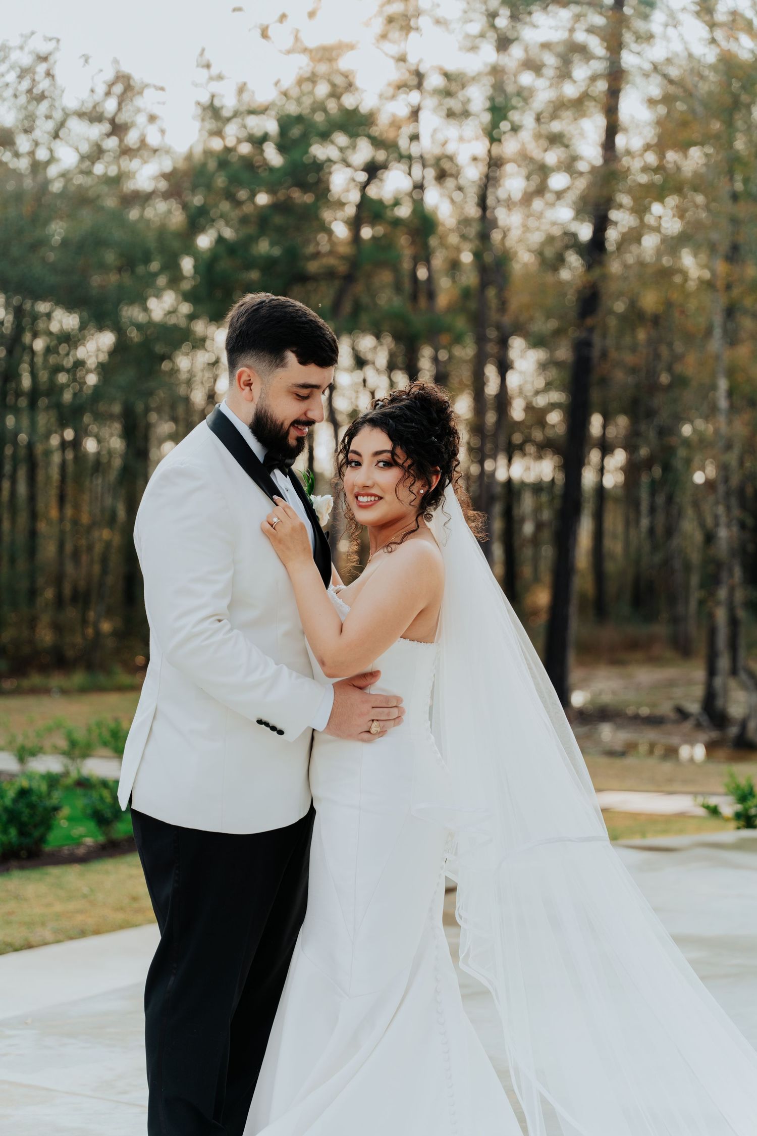 Wedding couple shares intimate dance moment outdoors in white formal attire.