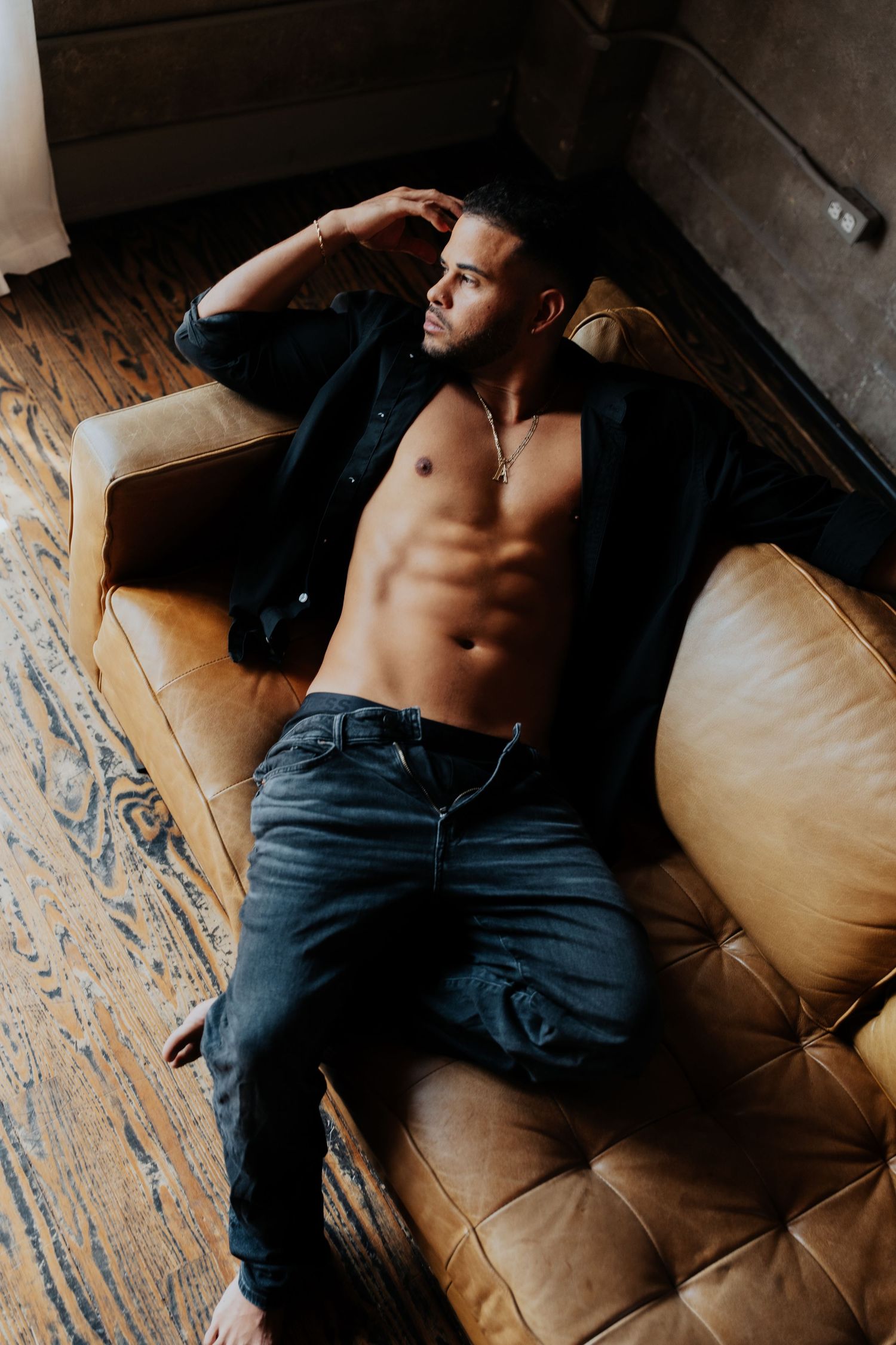 Artistic boudoir photo of person reclining on leather couch.