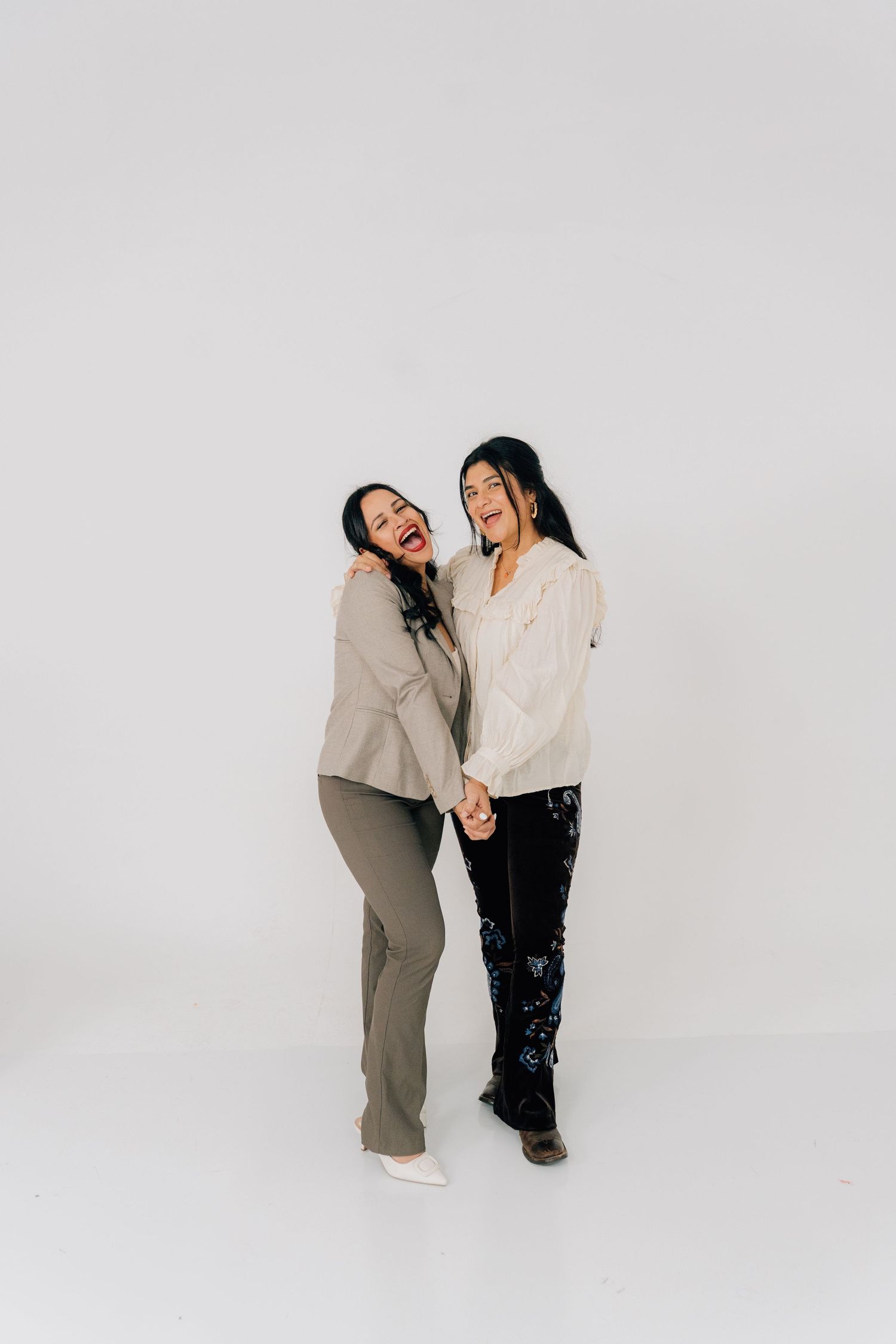 Two people laugh together during a casual studio photoshoot on white background.