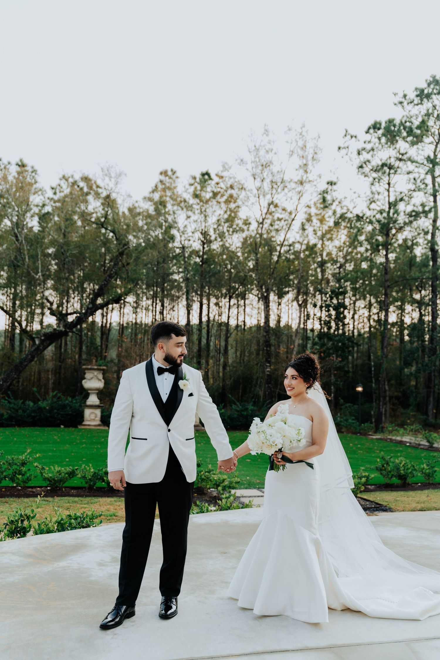 Bride and groom pose on outdoor patio with wooded backdrop in classic black and white attire.