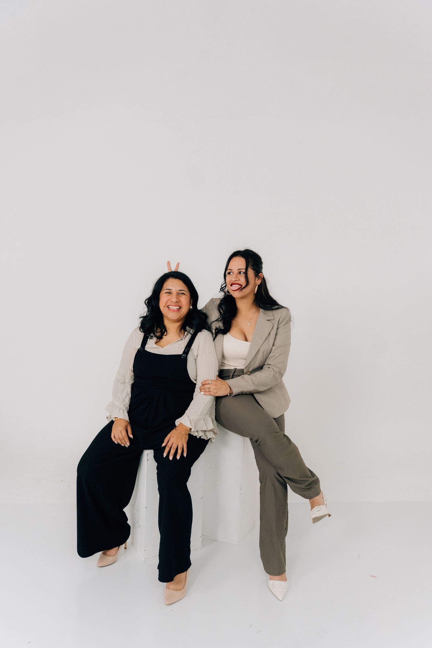 Two friends in casual wear share laughs while posing on a white studio floor.
