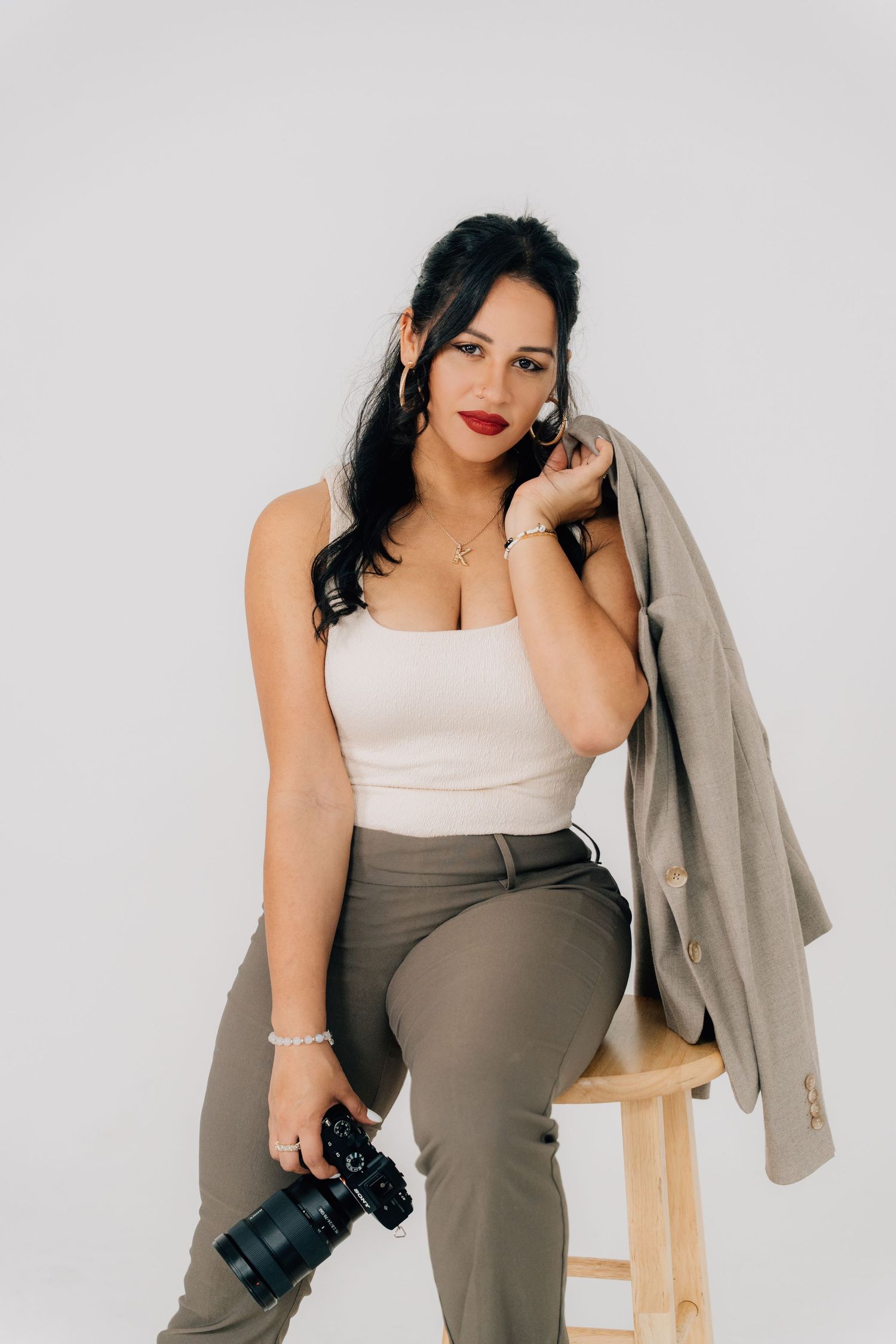 Professional photographer in neutral tones posing with camera against white background.