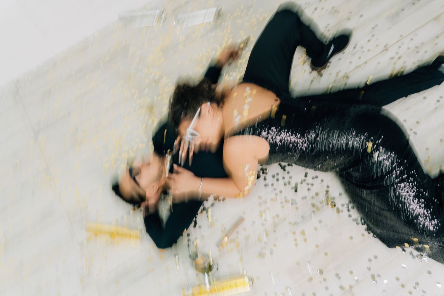 Artistic overhead shot of couple lying on white floor in formal attire.