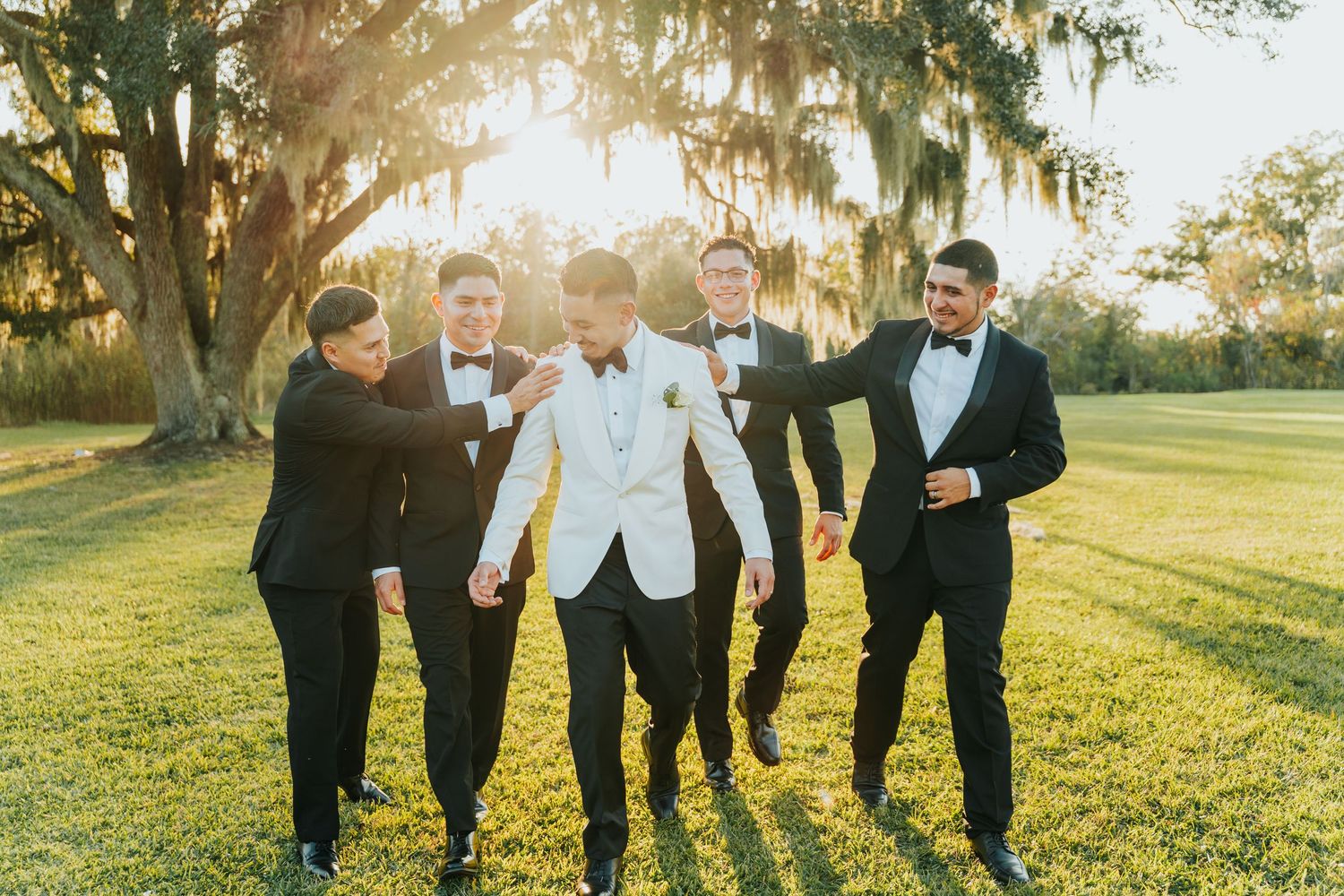 A group of people in formal attire walking together in a grassy field during golden hour sunset.