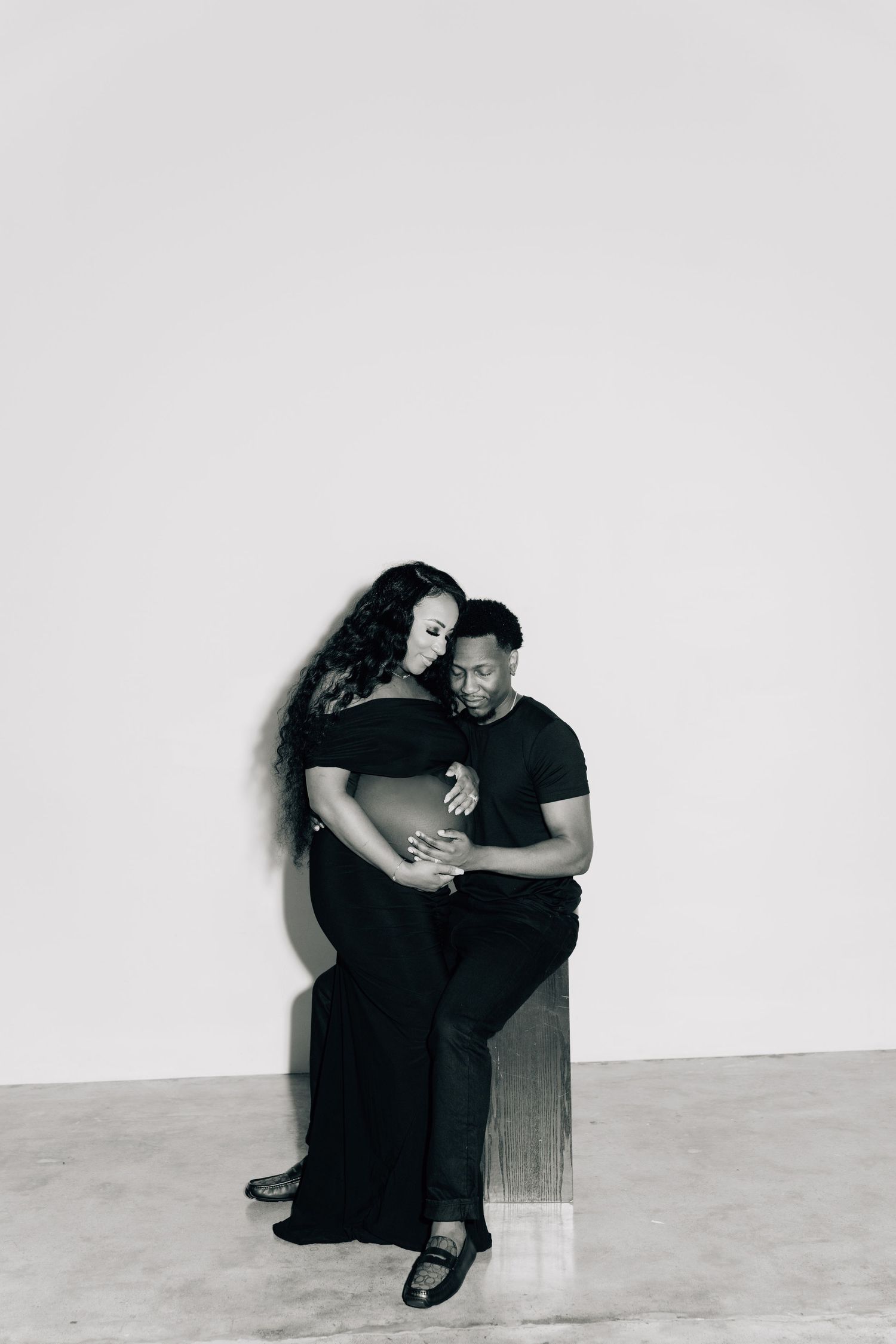 Minimalist black and white photos of a couple sitting against a white wall.