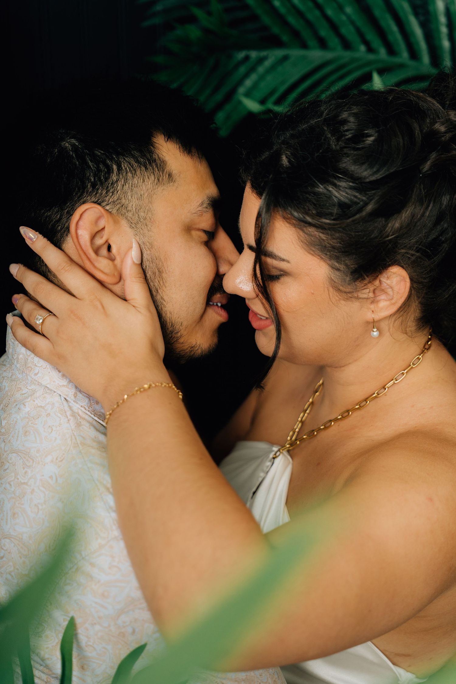 Intimate close-up of couple sharing tender moment against tropical palm leaf background.