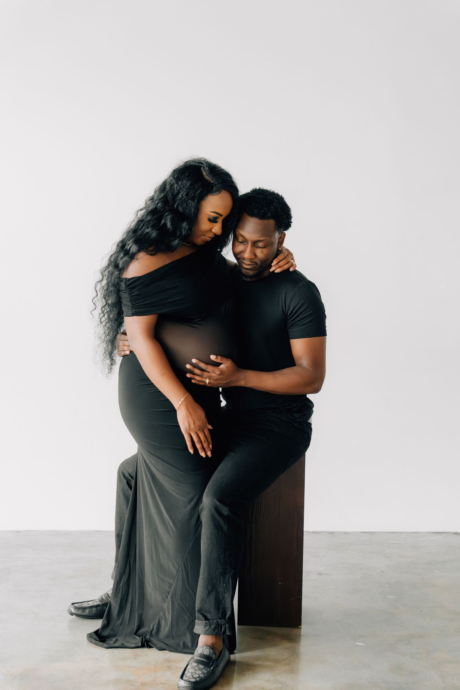 Maternity photo session with couple in black outfits against white backdrop.