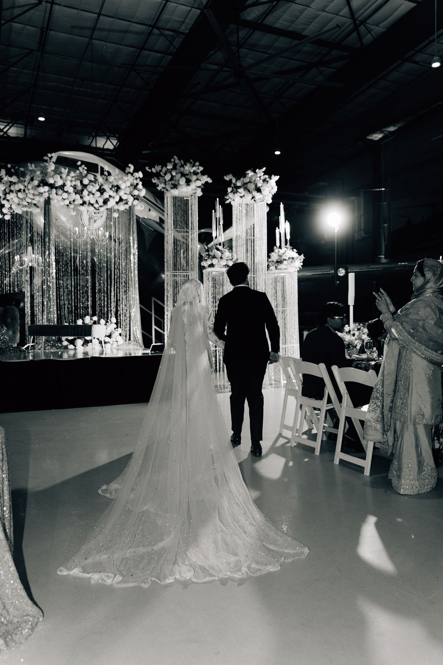 A wedding ceremony setup in an indoor venue with elegant white decor and floral arrangements.
