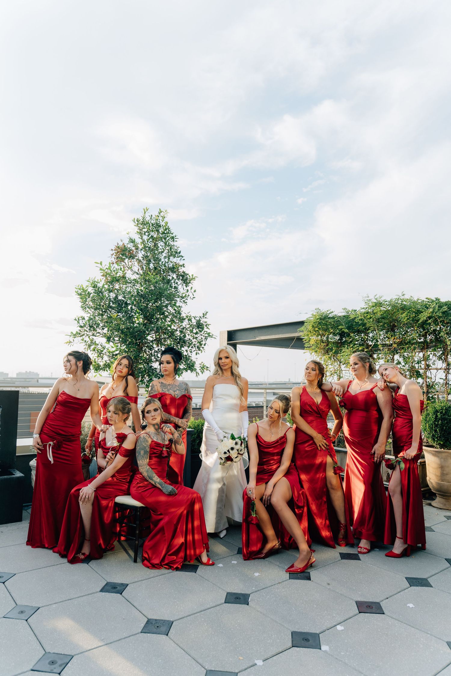Wedding party in red dresses posing together on outdoor rooftop terrace.