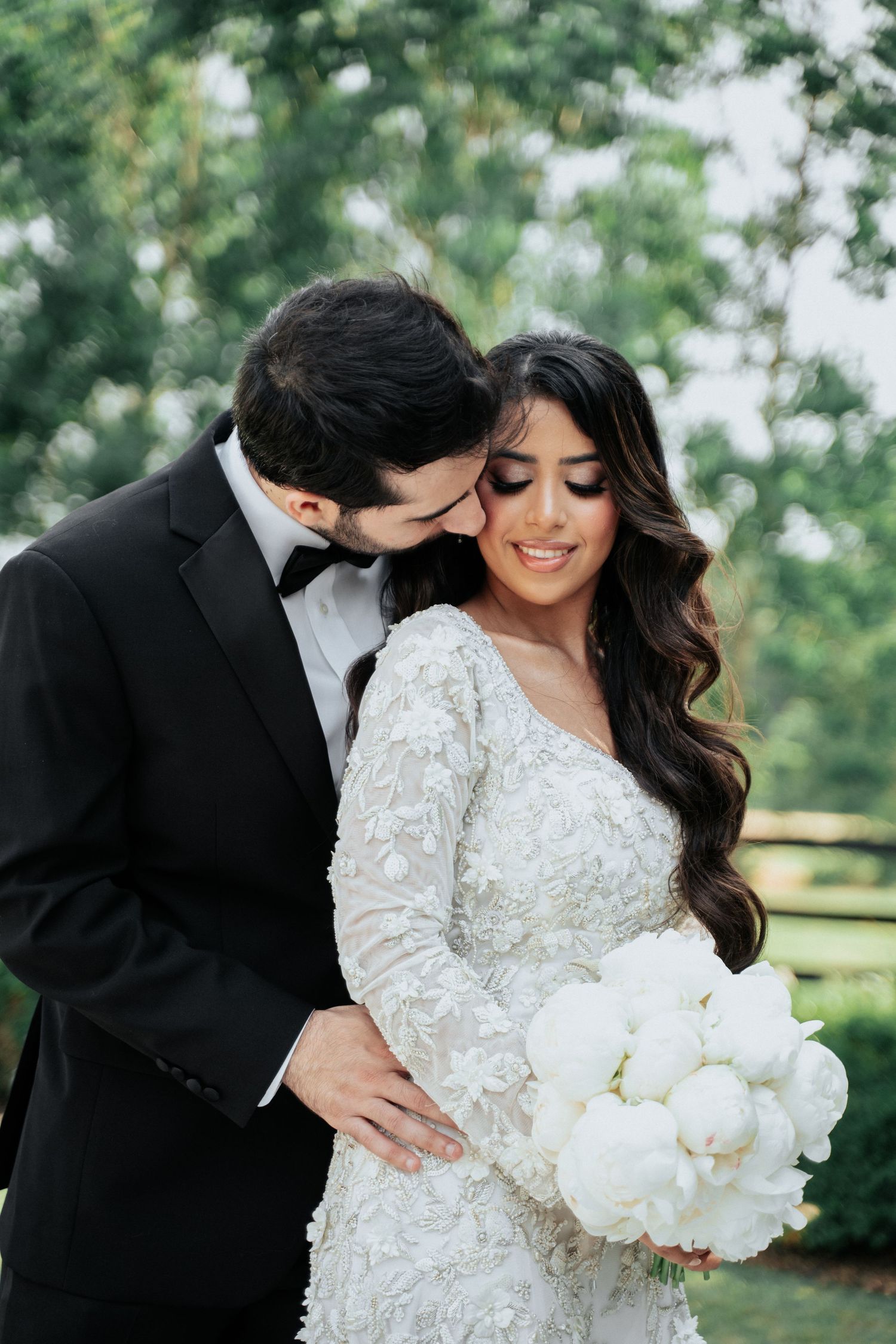 Romantic wedding portrait with couple embracing outdoors in formal attire.