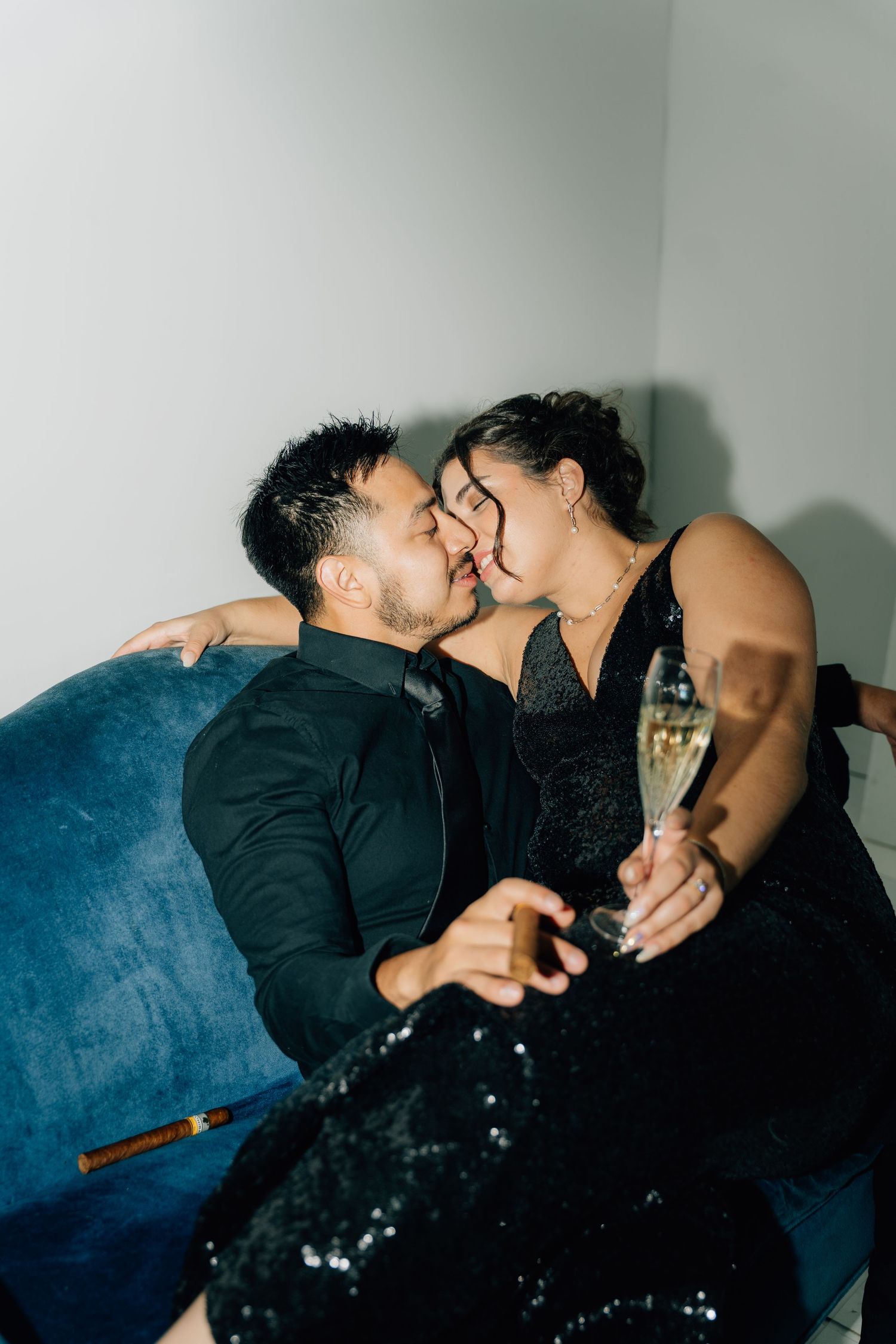 Couple sharing intimate moment on blue velvet couch with champagne glass.