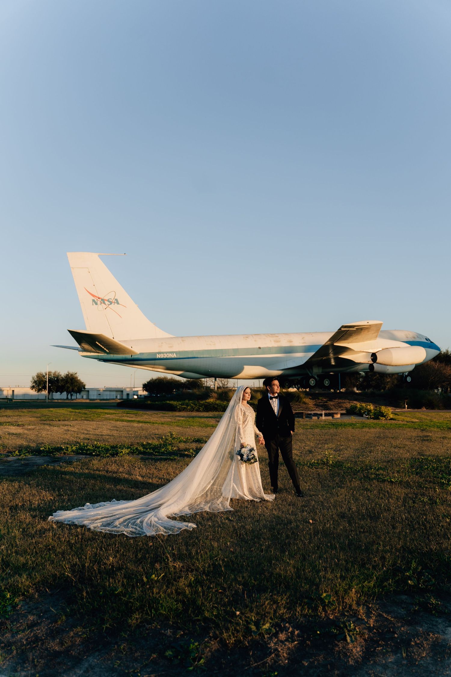 Wedding couple poses for photos near a large white airplane at sunset.