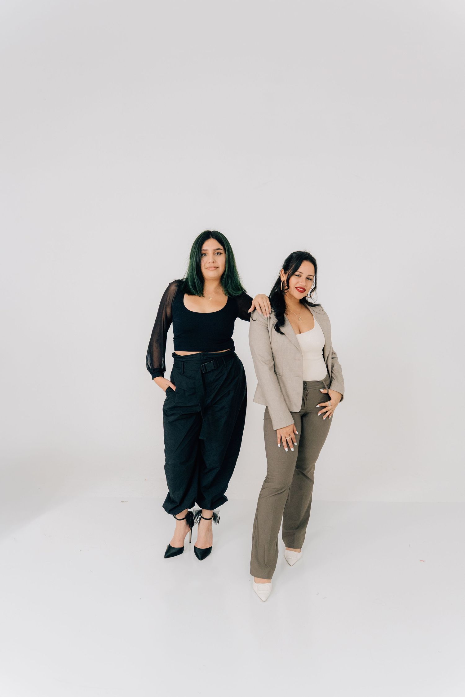 Two people in black and beige outfits pose dynamically in a minimalist studio setting.