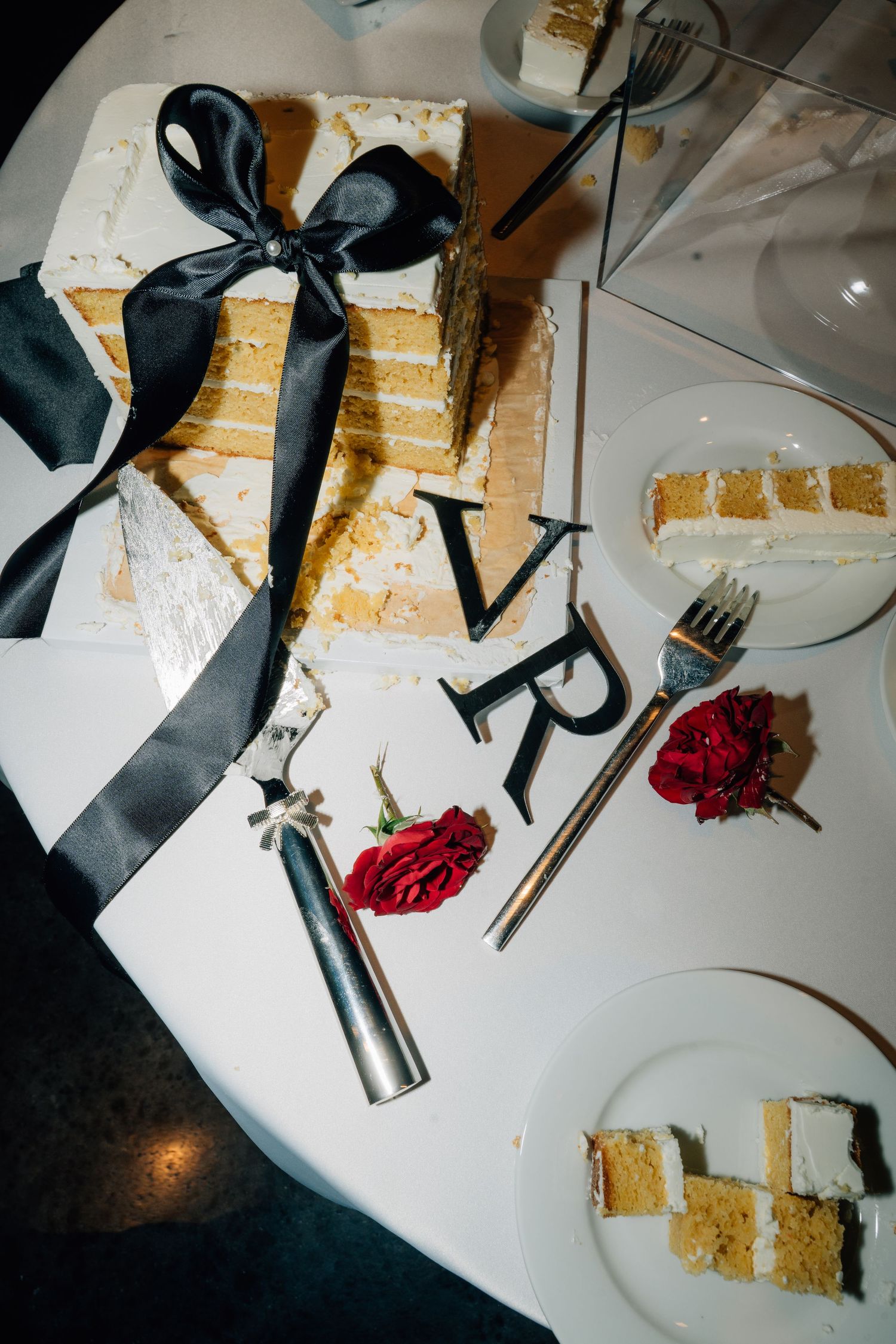 Wedding reception table details with black accessories and cake pieces on white tablecloth.