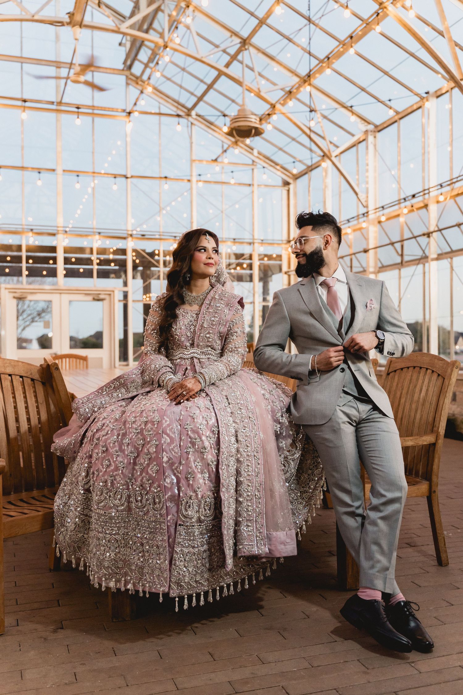 Couple sitting in a greenhouse, wearing elegant formal attire.