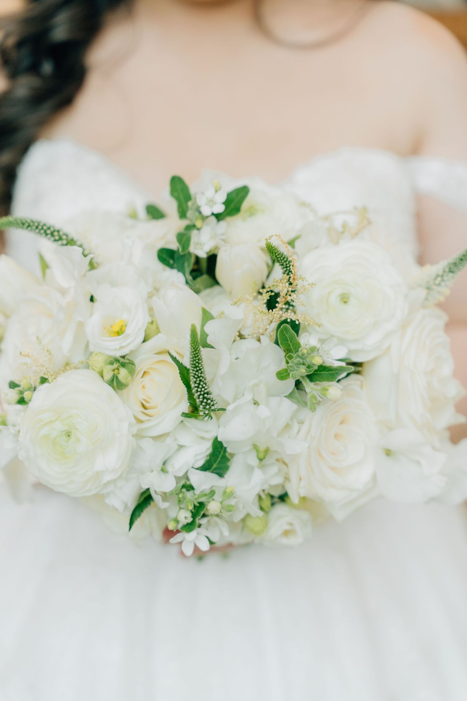 An elegant white wedding bouquet with roses and greenery against a bridal gown.
