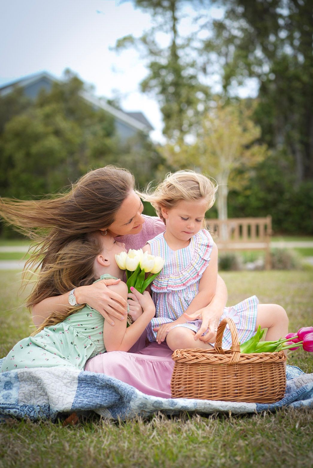Mother and two daughters enjoy a spring picnic on grass, sharing tulips and a wicker basket outdoors.