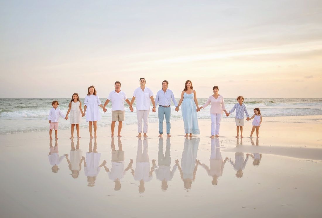 Group silhouettes walking together on beach at sunset with reflections in wet sand.