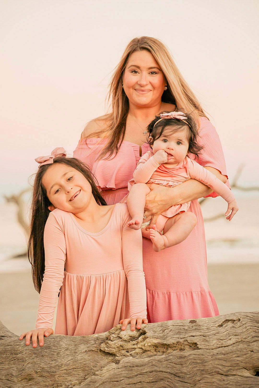 A series of beach portraits showing playful poses in matching pink dresses against a sandy backdrop at sunset.