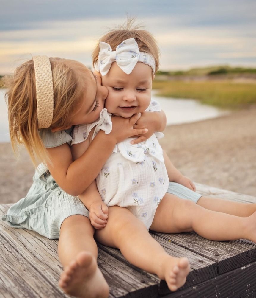 Sweet candid moment between siblings on wooden dock by the water.