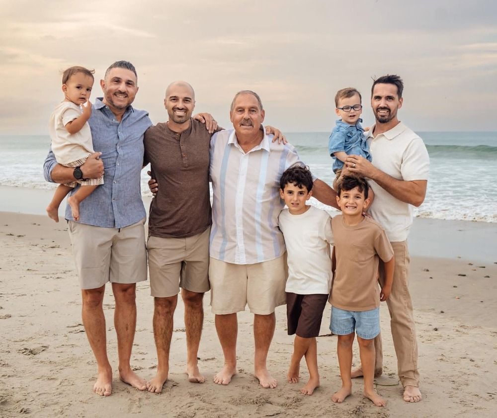 Extended family members stand in line showing their feet on sandy beach.