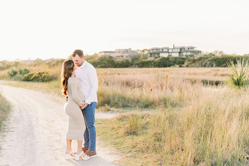 Couple walking through coastal dunes with beach houses visible in the background.