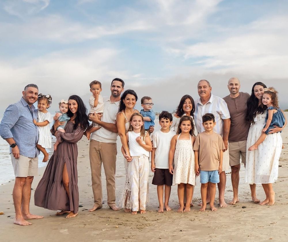 Panoramic view of extended family posing together on beach in coordinated outfits.
