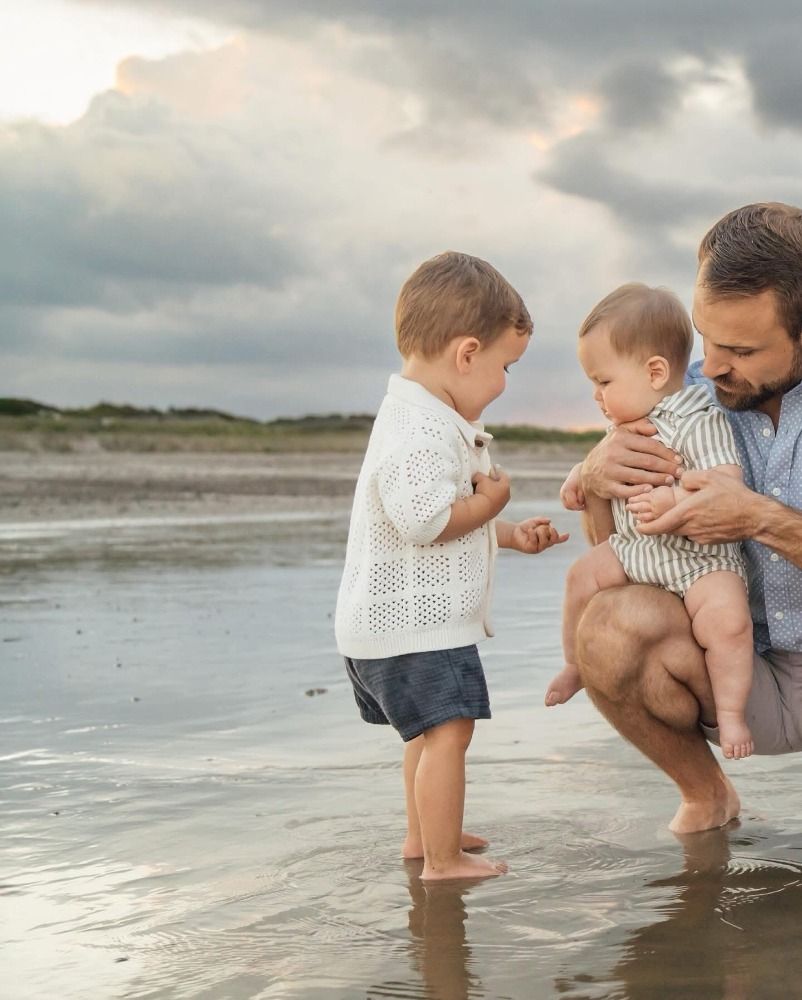 Family sharing tender moments while playing in shallow ocean water at sunset.