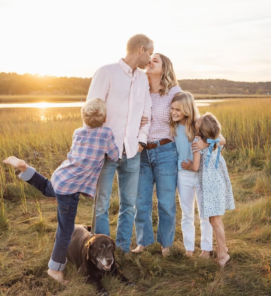 Family portrait at sunset in a grassy field with their chocolate lab.