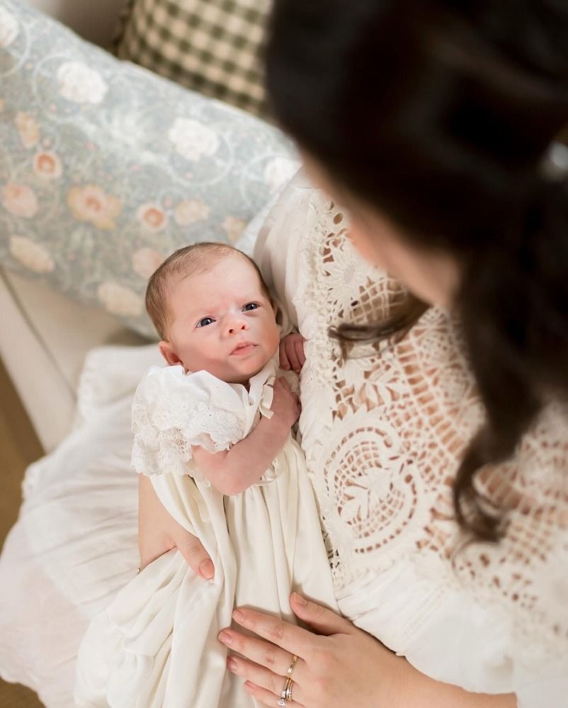 Delicate lace details and newborn baby in white christening gown.