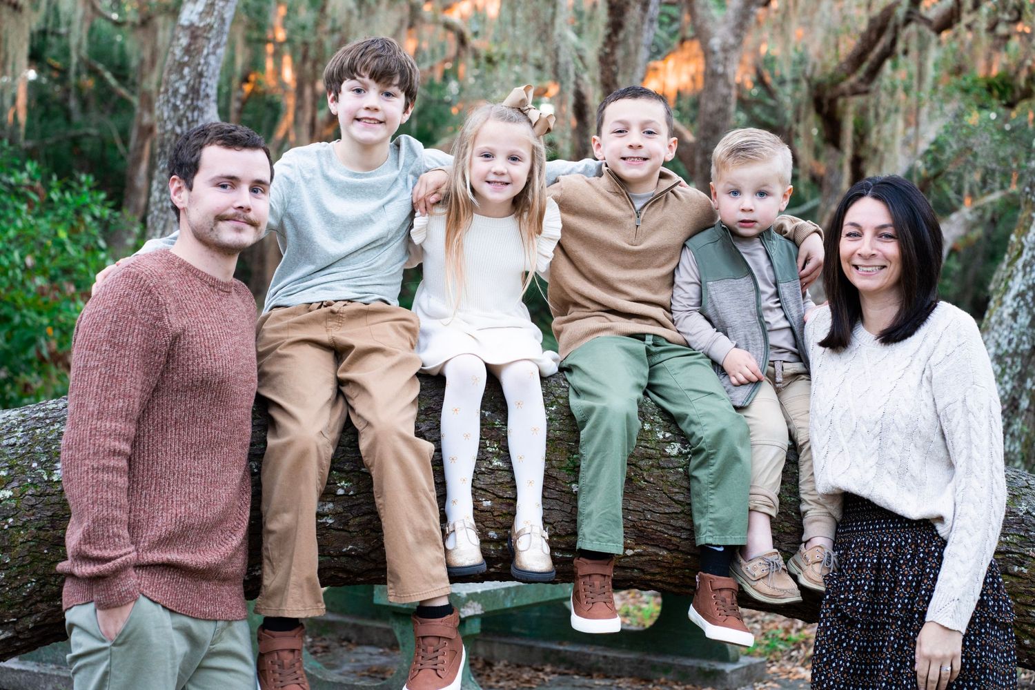 A group of people in coordinated casual outfits pose together outdoors against a natural backdrop.