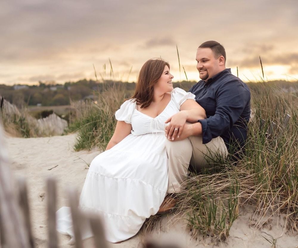 Romantic couple lounging on sand dunes during golden hour sunset at the beach.