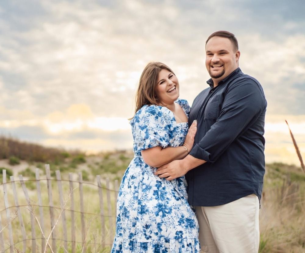 Couple in coordinated blue and white outfits sharing joyful moments on coastal dunes.