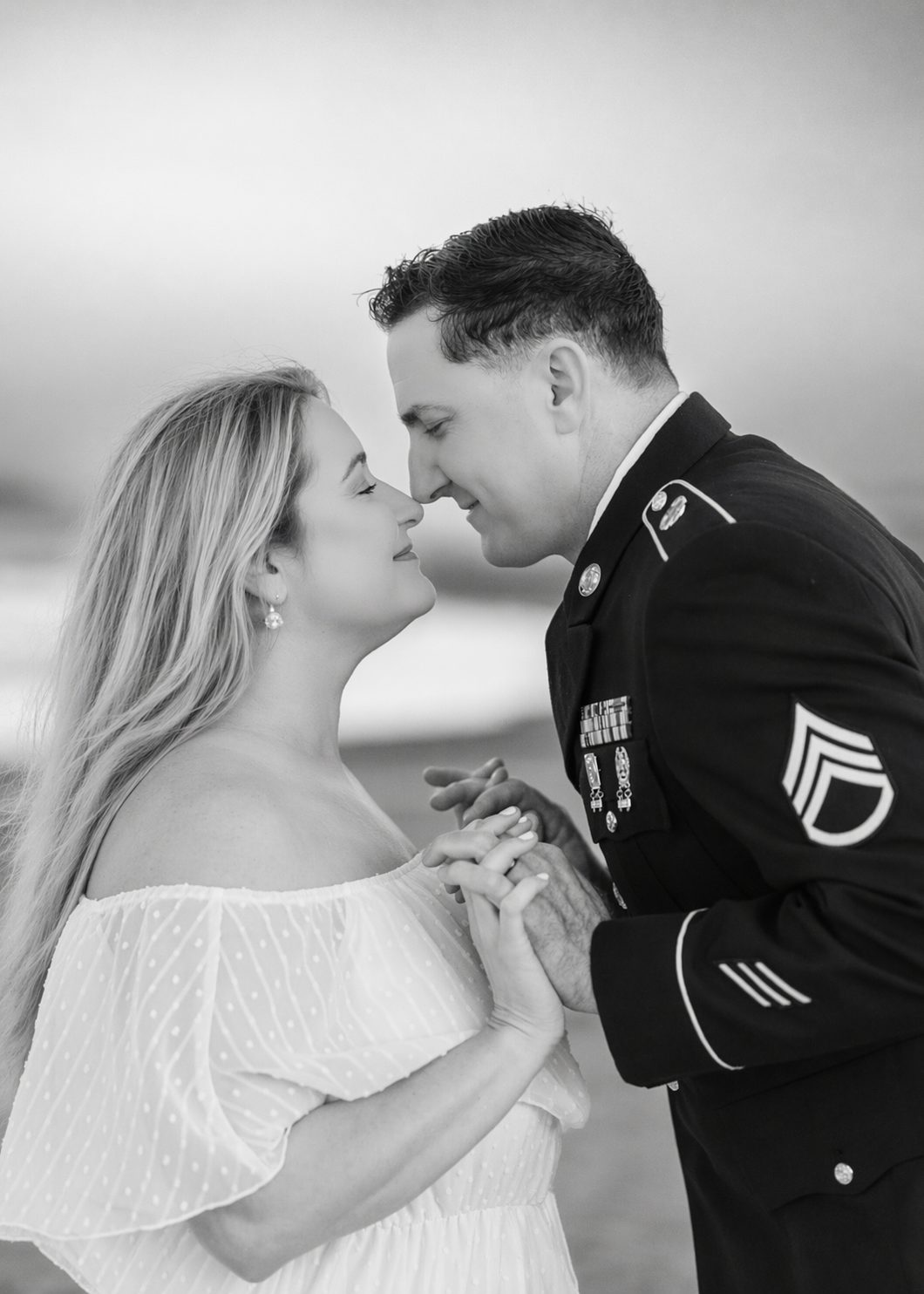 Black and white photo of a military man in dress uniform about to kiss a woman in a white off-shoulder dress.