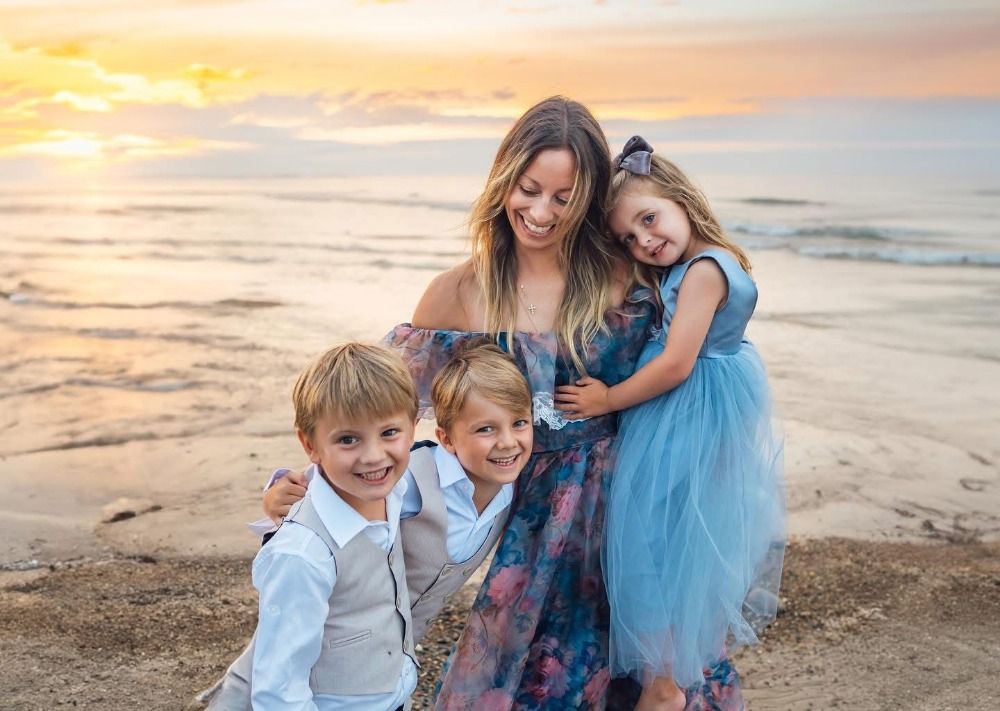 Family in coordinated blue and white outfits playing together on beach at sunset.
