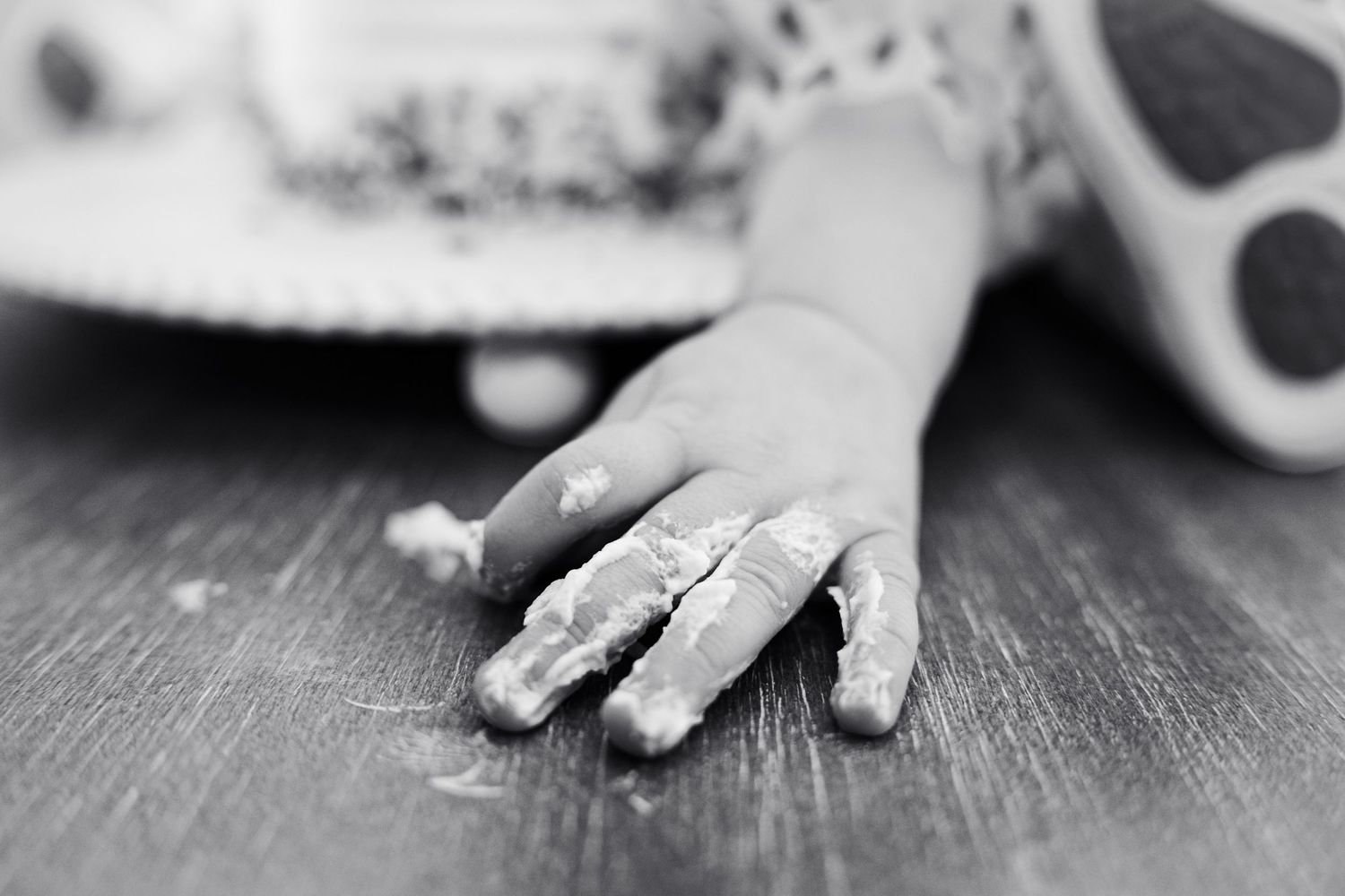 Black and white photo of a baby hand covered in cake frosting resting on a wooden surface.