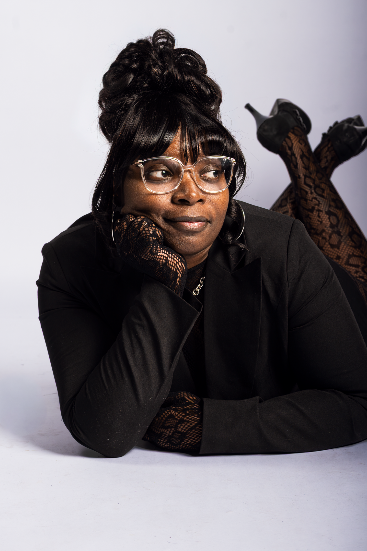 Person wearing glasses and black sweater poses on floor in studio setting.