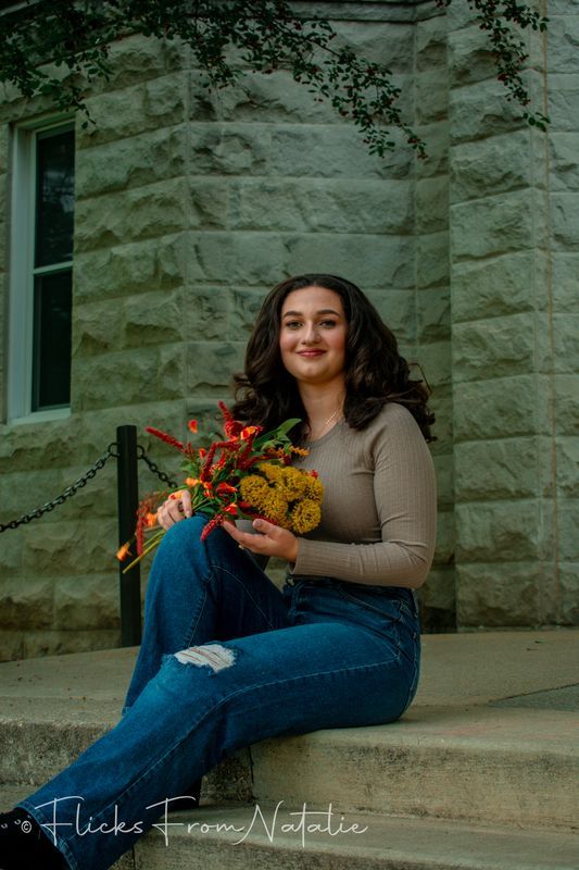 Person relaxes on stone steps with autumn flowers in casual photoshoot.