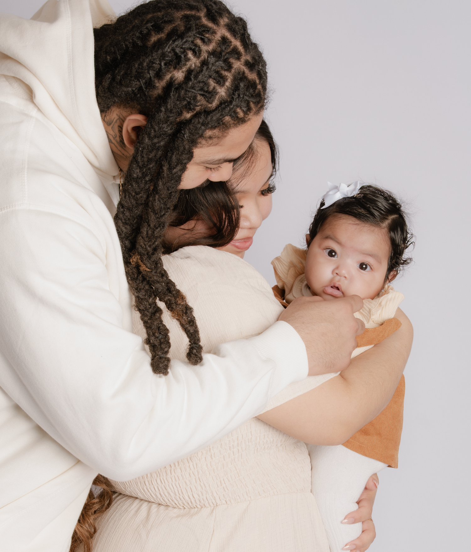 A parent with braided hair tenderly holds a baby dressed in orange, sharing an intimate family moment.
