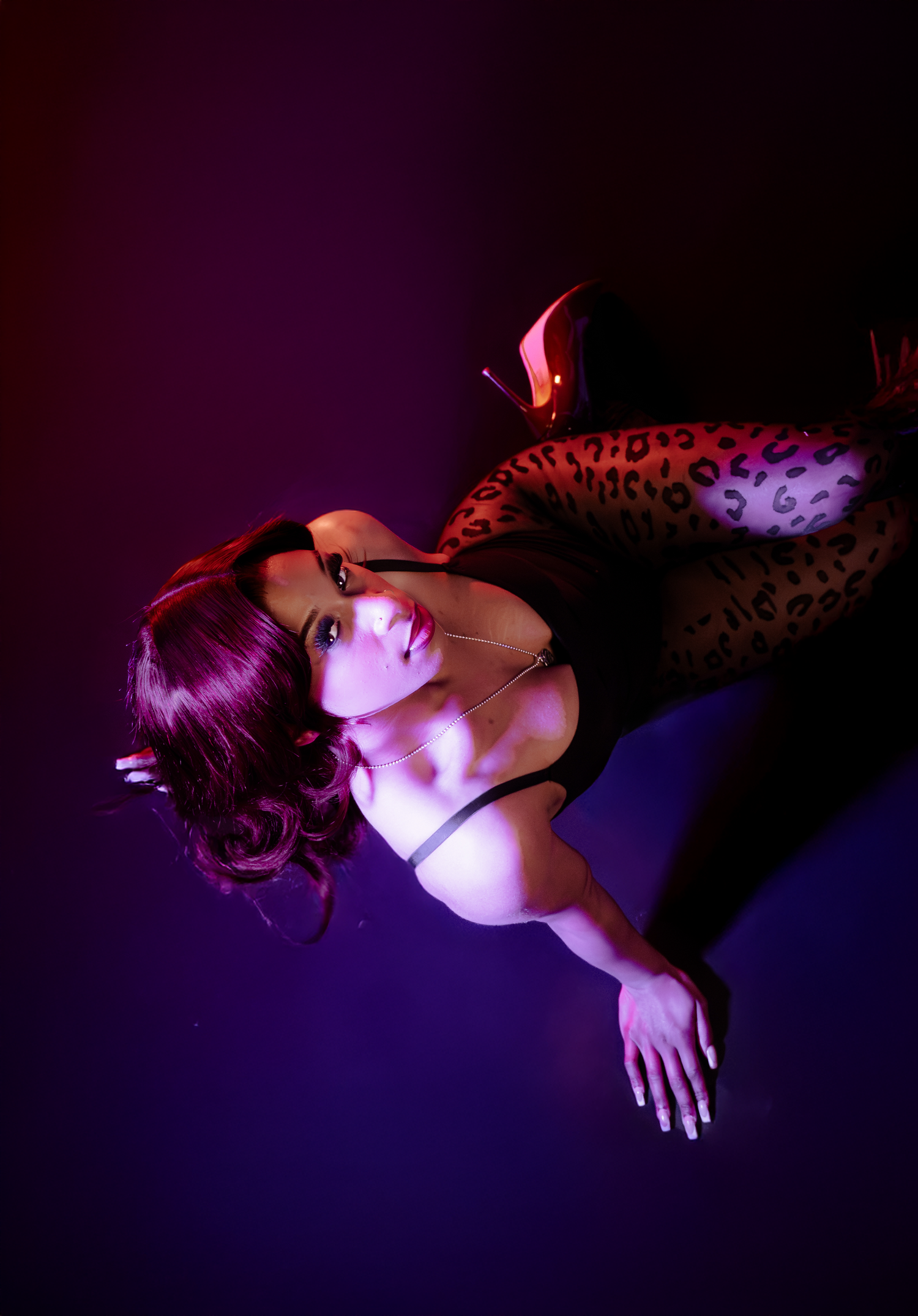 Artistic portrait with purple lighting shows figure in dramatic reclining pose.