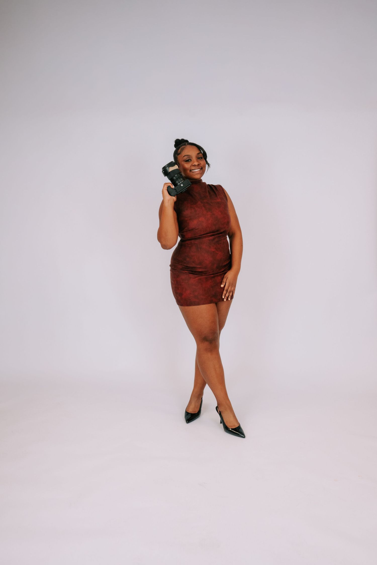 Woman in burgundy mini dress and black heels poses confidently holding a green kettlebell in a studio.